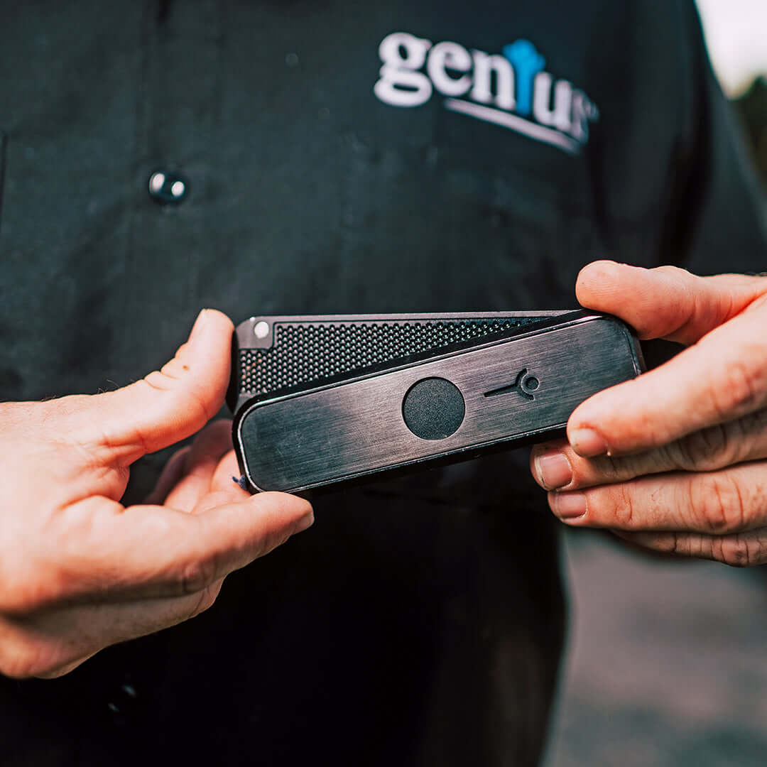 Hands holding Genius Pipe Mini Black with slider skewed off-center.